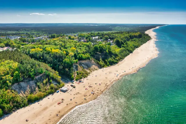 Słoneczna plaża w Jastrzębiej Górze z turkusowym morzem i zielonymi klifami. Idealne miejsce na rodzinne atrakcje dla dzieci.